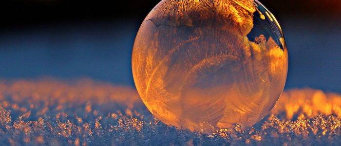 Close-up shot of a frozen bubble with warm reflections resting on a snowy surface at twilight.